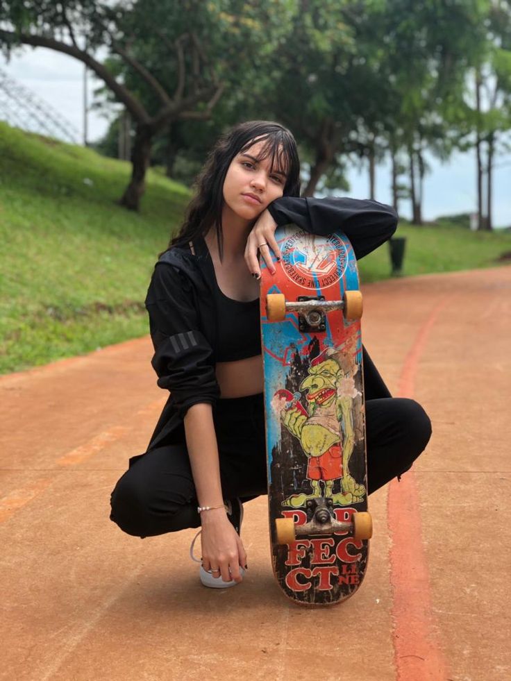 a woman kneeling down with her skateboard on the ground in front of her,