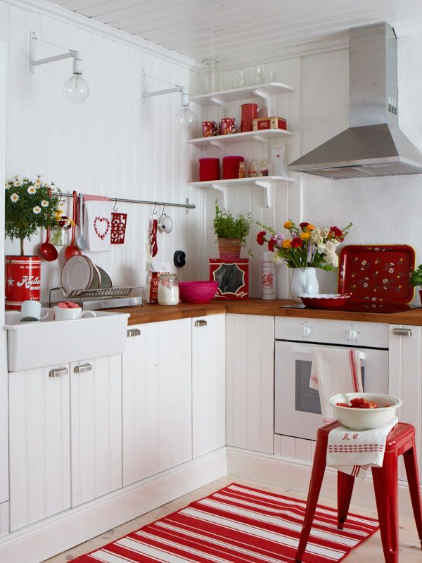 a kitchen with red and white accessories on the counters, shelves, and rugs