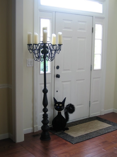 a black cat sitting on the floor in front of a white door with a candelabra next to it