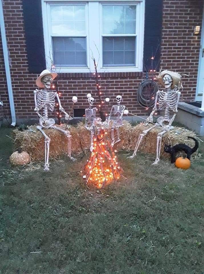 three skeletons sitting on hay bales in front of a house decorated with lights and pumpkins