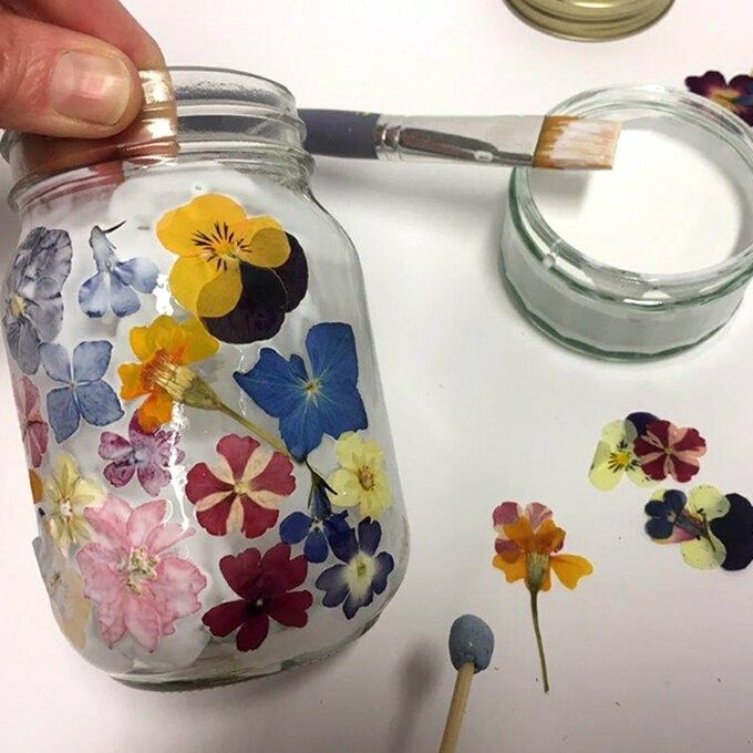 a person is painting flowers on a glass jar