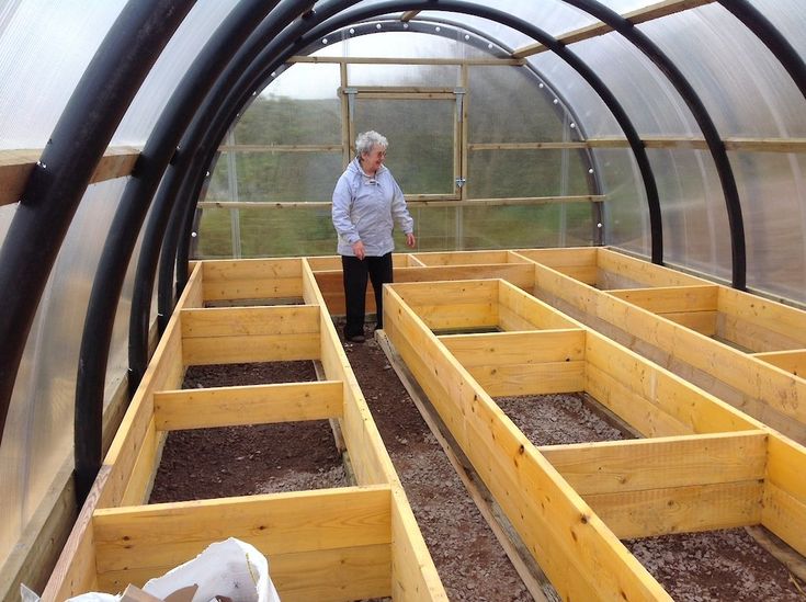 an older woman standing in a greenhouse with lots of wooden boxes on the ground next to her