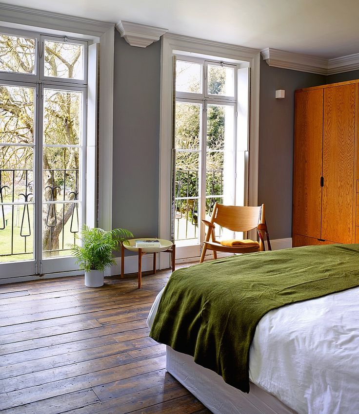 a bedroom with wooden floors and green blankets on the bed in front of two large windows