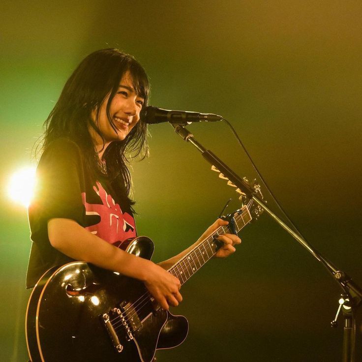 a man with long hair playing guitar and singing into a microphone on stage at a concert