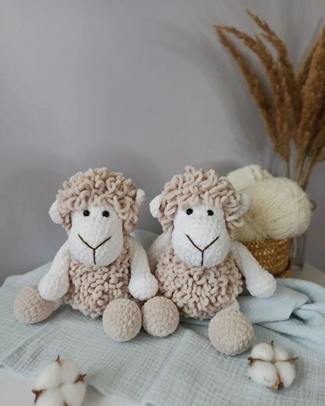 two stuffed sheep sitting next to each other on a table with yarn and flowers in the background