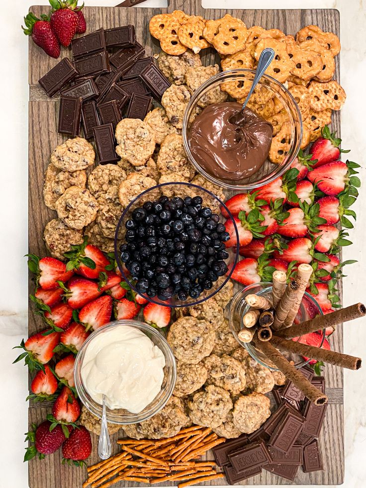 a wooden platter filled with cookies, strawberries and other snacks on top of it