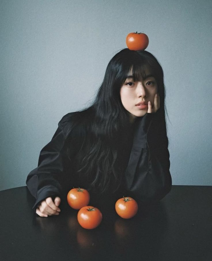 a woman sitting at a table with four tomatoes on her head and one tomato atop her head