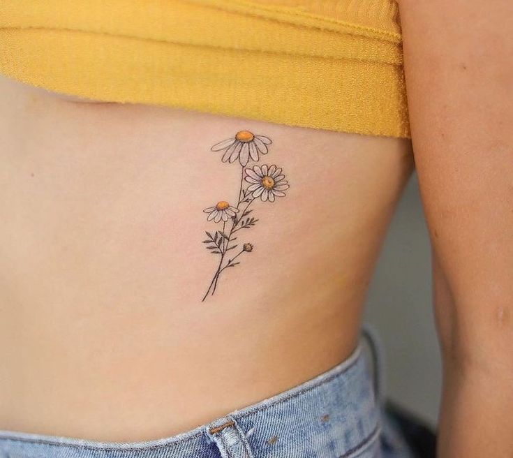 a woman's stomach with daisies tattoo on her left side ribcage