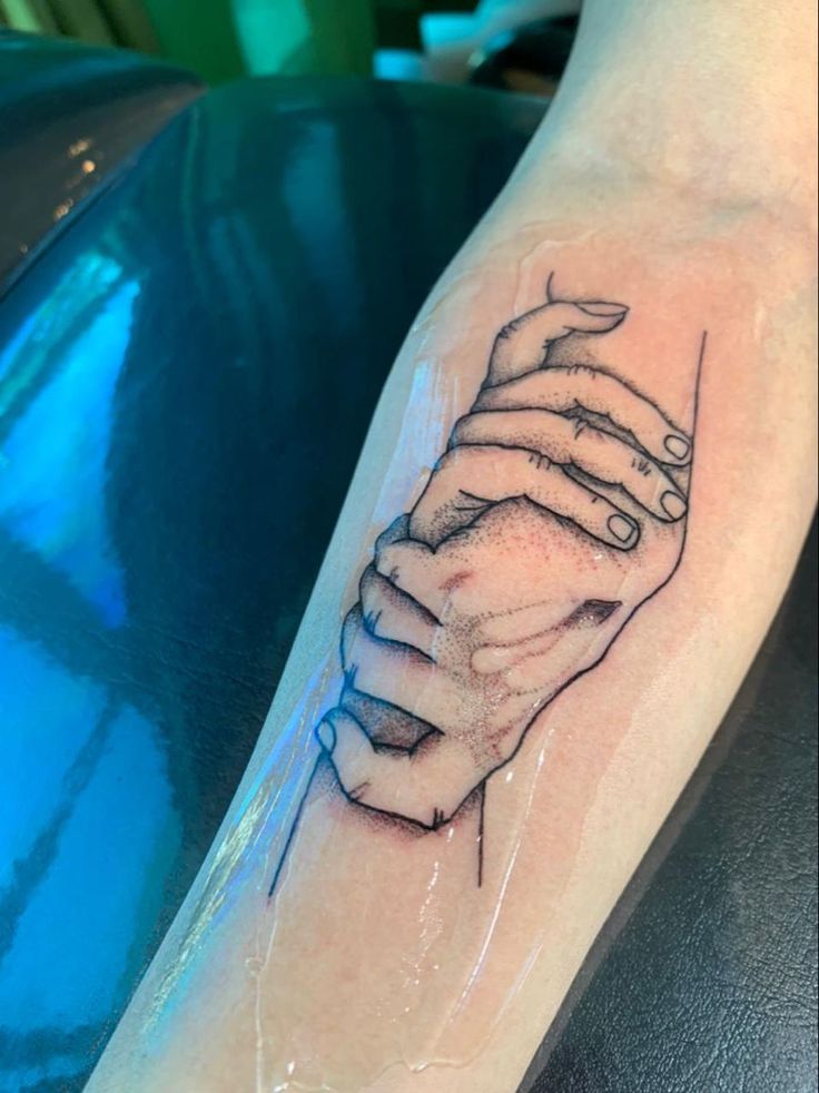 a tattoo on the arm of a person with two hands holding each other in black ink