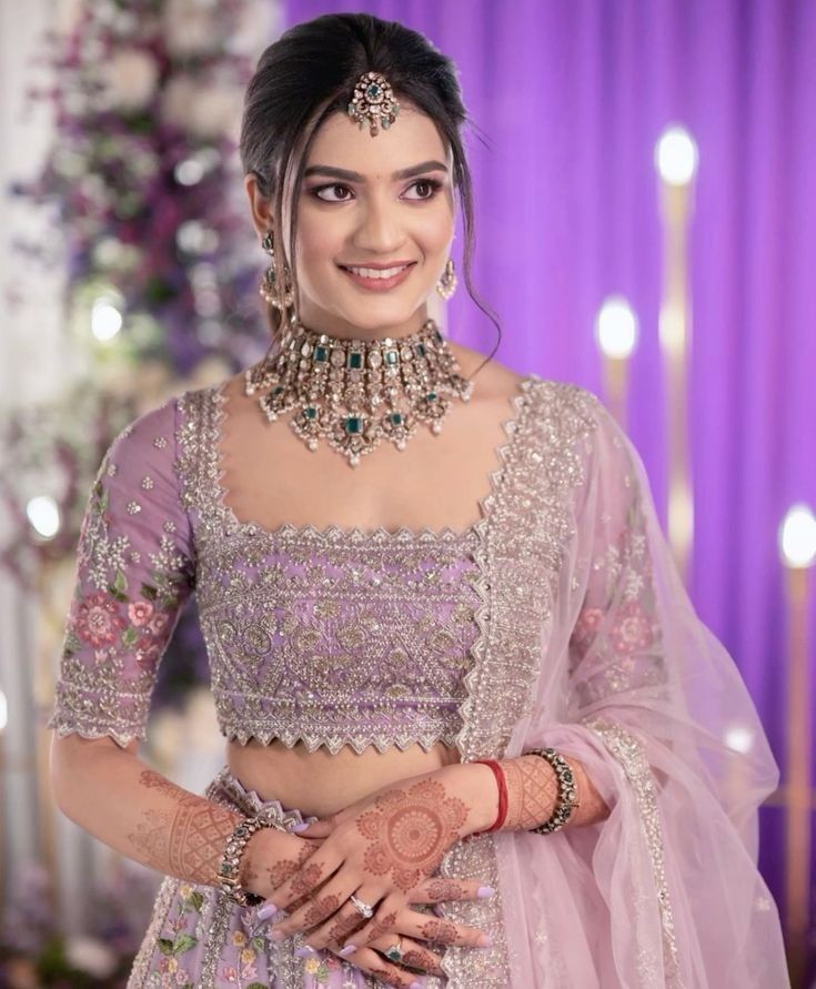 a woman in a pink lehenga with jewelry on her neck and hands behind her back