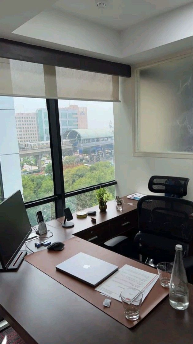 an office desk with a laptop computer on top of it next to a large window