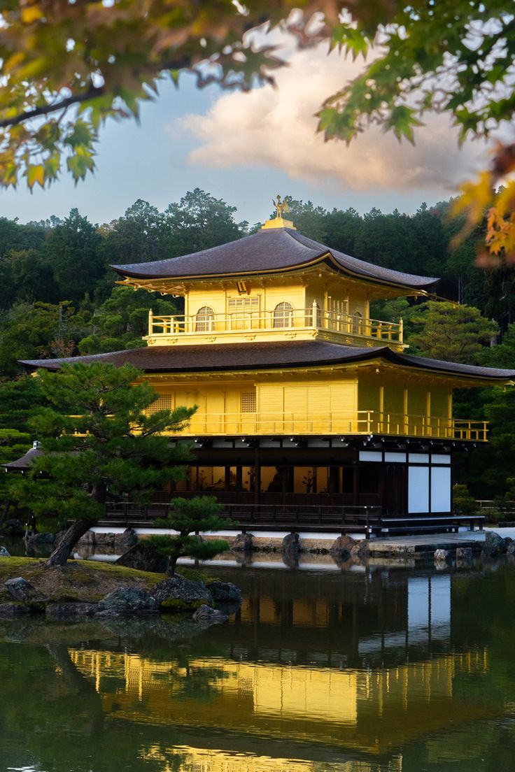 a yellow building sitting on top of a lush green hillside next to a lake and forest