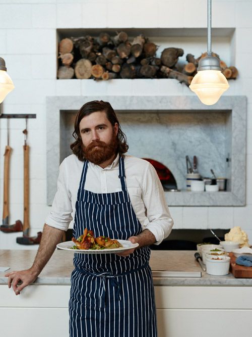 a man with a beard holding a plate of food in front of a fire place