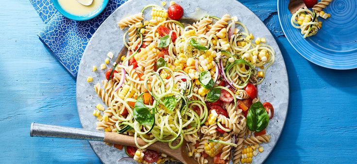 a plate of pasta with corn, tomatoes and spinach on a blue wooden table