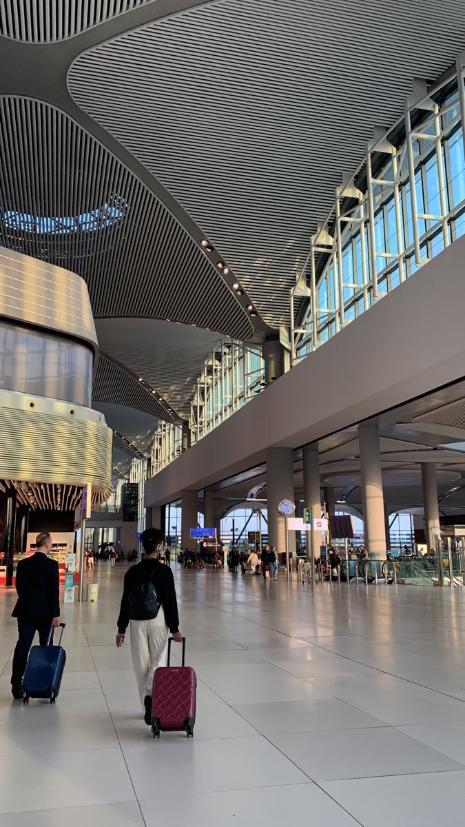 two people walking through an airport with their suitcases in front of the terminal entrance