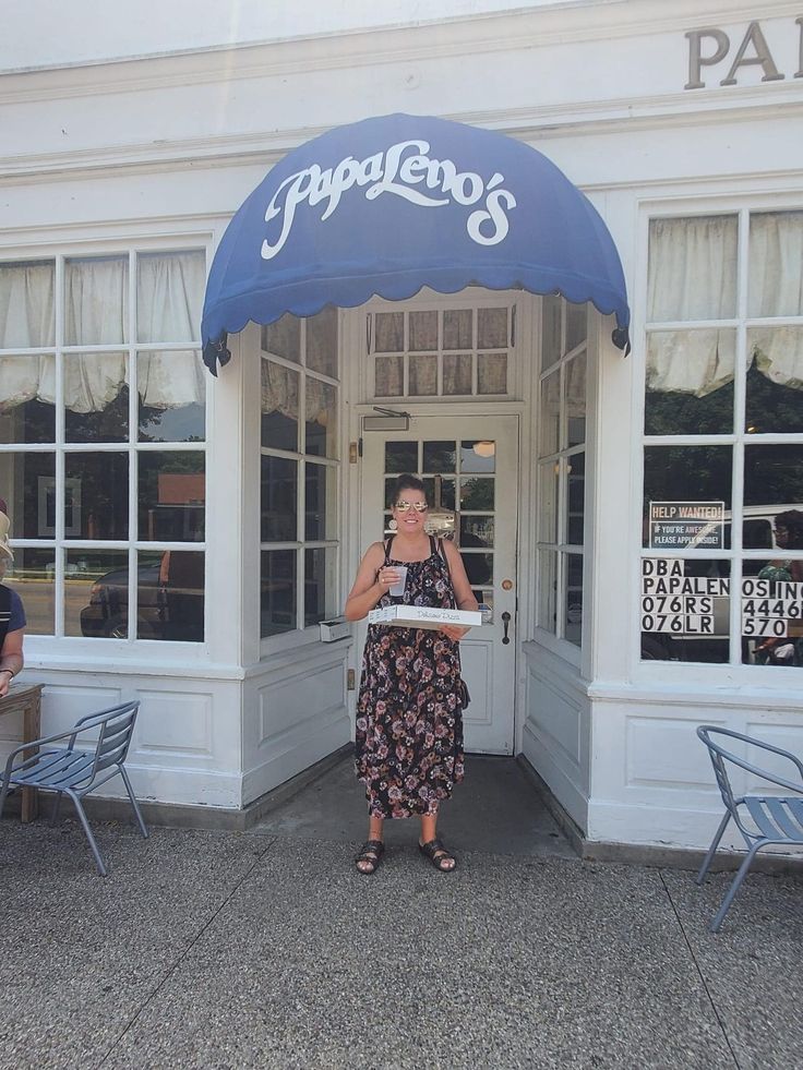 a woman standing in front of a restaurant with blue awnings on the entrance