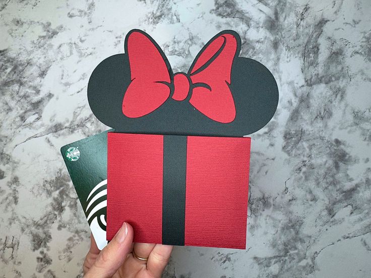 someone is holding up a card with a minnie mouse head on it and a red bow