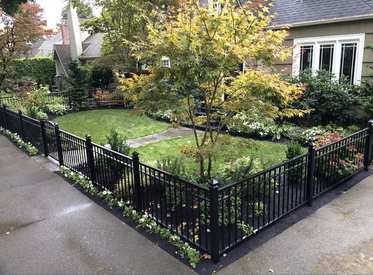 a fenced in yard with trees and flowers on the side of it next to a house