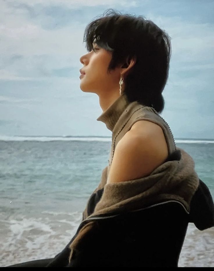 a woman standing on top of a sandy beach next to the ocean with her hair in a bun