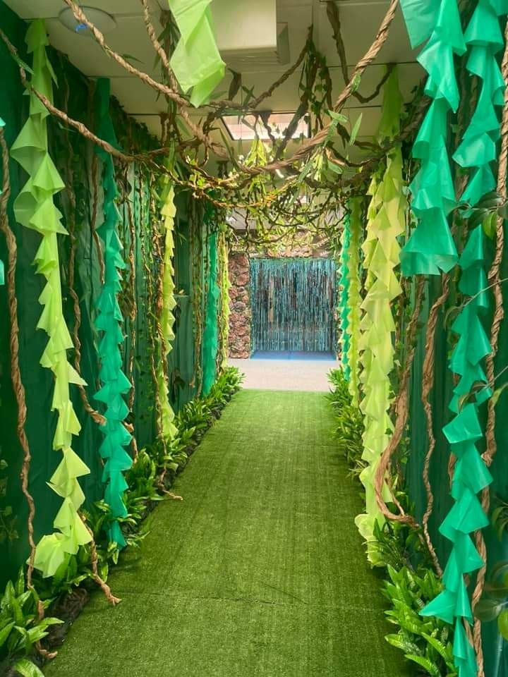 an outdoor walkway decorated with green and yellow paper garlands, grass and plants on either side