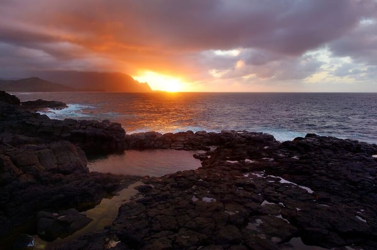 the sun is setting over an ocean with rocks