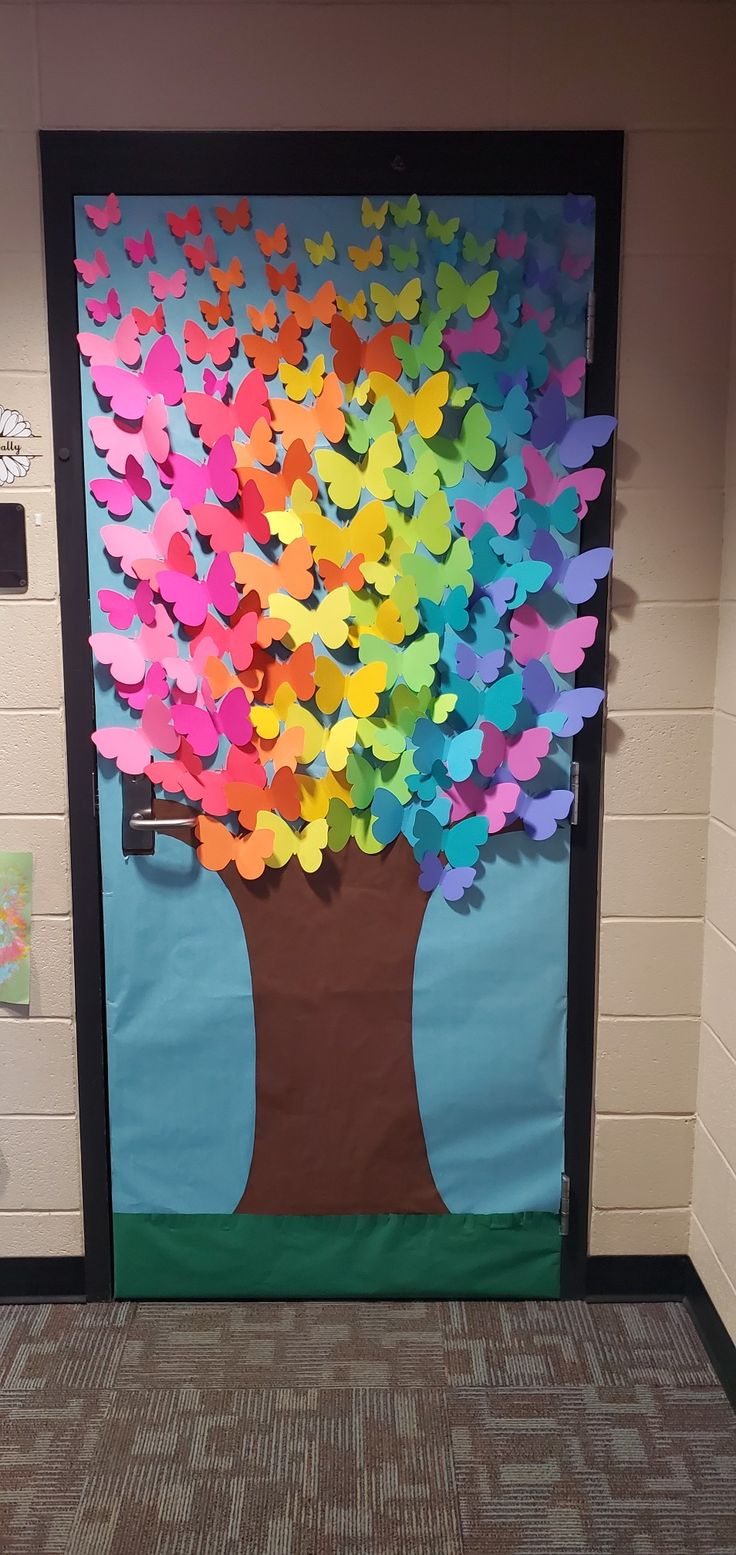 a classroom door decorated with paper butterflies and a tree made out of colored paper hearts