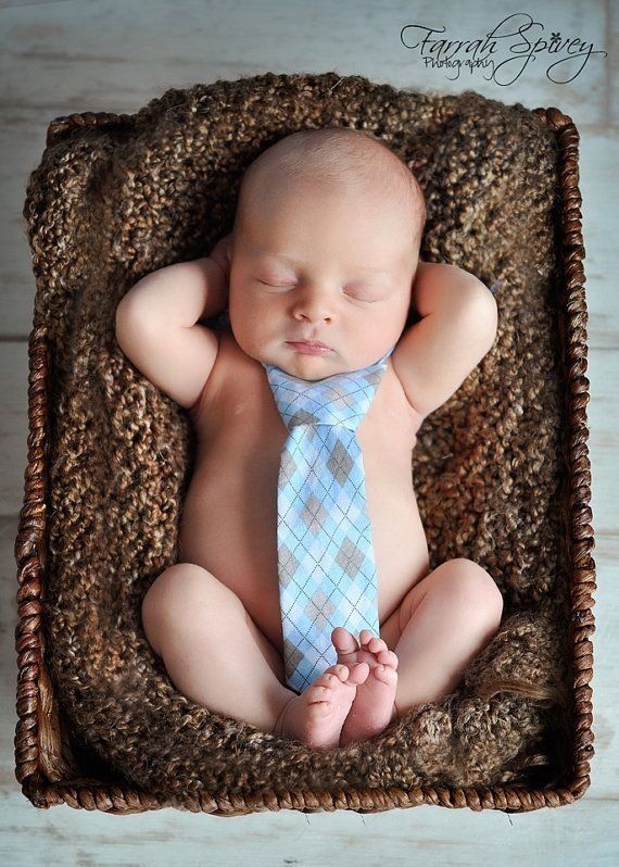 a baby wearing a blue tie laying on top of a brown blanket in a basket