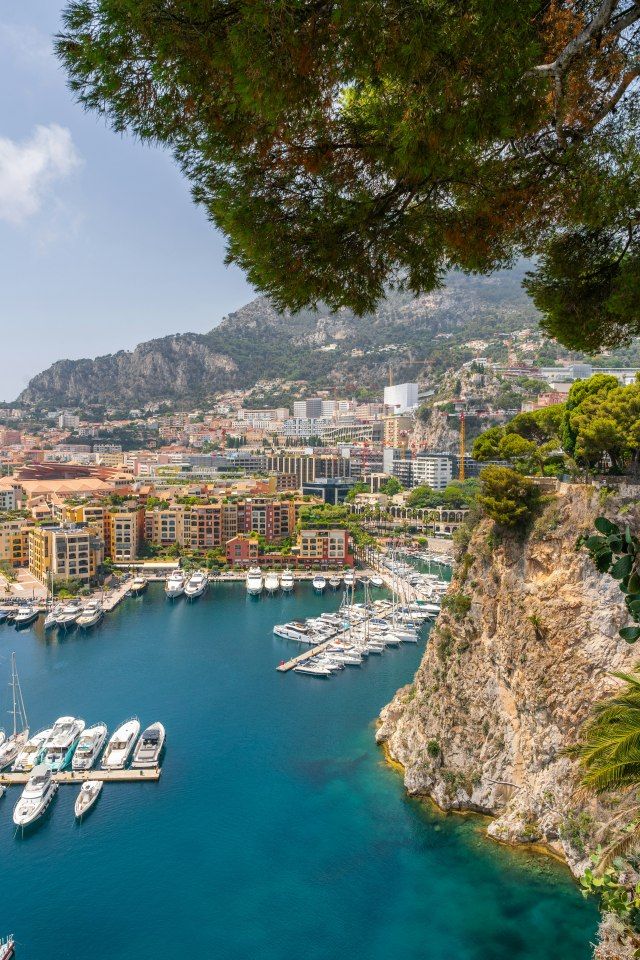 boats are docked in the blue water next to some cliffs and buildings on either side