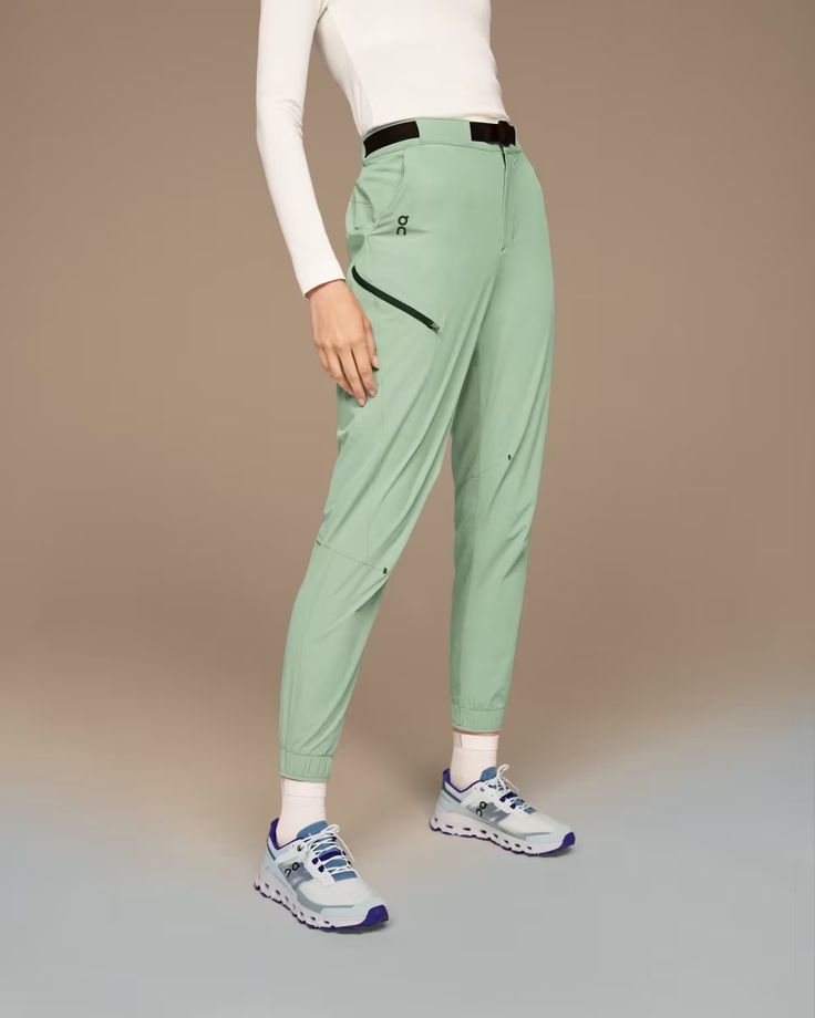 a woman in white shirt and green pants with sneakers on her feet, posing for the camera