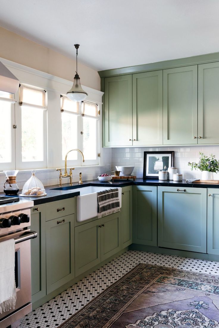 a kitchen with green cabinets and black counter tops, an area rug on the floor