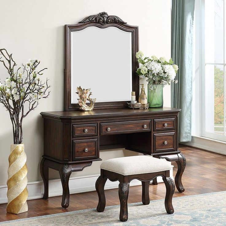 a wooden vanity with mirror, stool and flowers in vases on the floor next to it