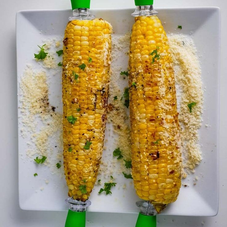 two corn cobs on a white plate with parmesan cheese and seasoning