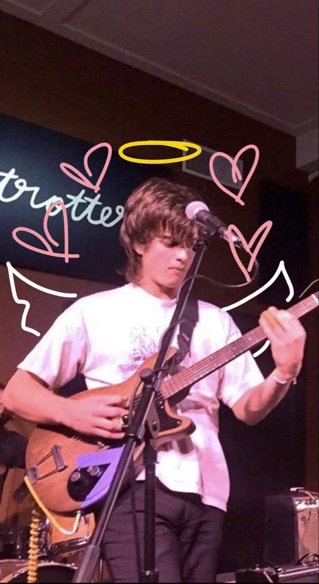 a young man playing guitar on stage with a microphone in front of him and an i love you sign behind him