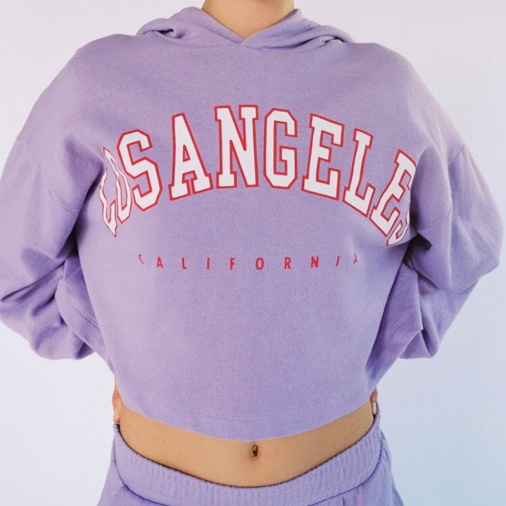 Varsity Jogger Sweatshirt Lilac Los Angeles, Ca Graphic Size Small Sweater With Hood, Cropped Brand New With Tags Trendy Lavender Winter Tops, Trendy Lavender Tops For Winter, Trendy Purple Sweatshirt With Ribbed Cuffs, Purple Tops With Ribbed Cuffs For Streetwear, Purple Letter Print Sweater For Fall, Trendy Lavender Cotton Sweatshirt, Casual Hooded Purple Sweater, Casual Purple Hooded Sweater, Casual Lavender Sweatshirt For Spring