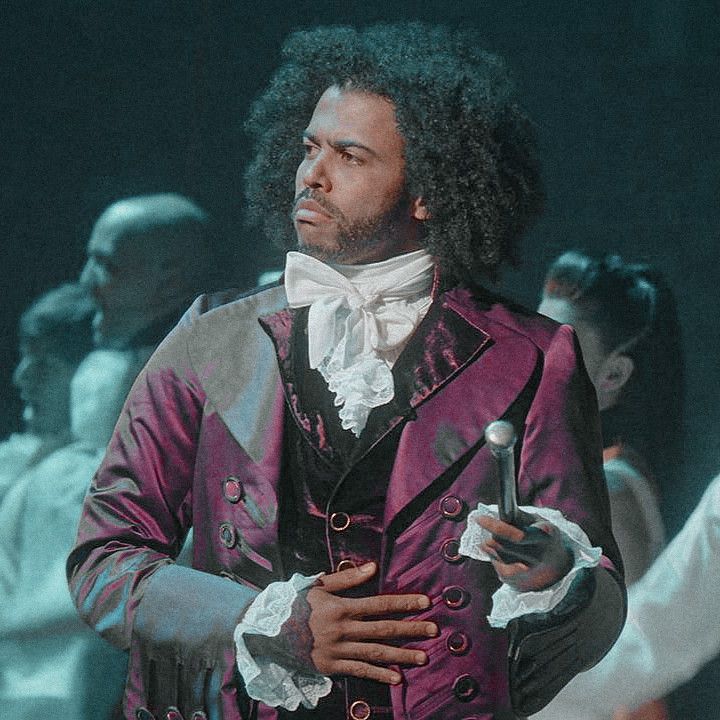 a man with long hair wearing a purple suit and holding a pipe in his left hand