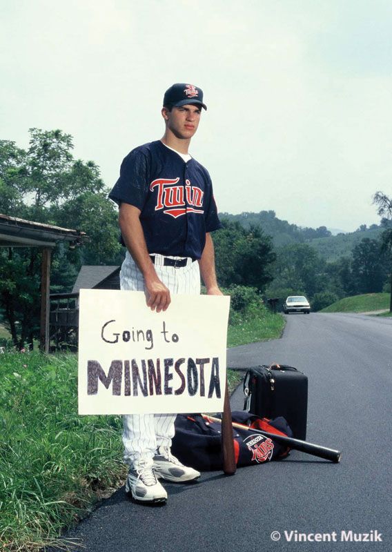 a man holding a sign standing next to a baseball bat and bag on the side of the road