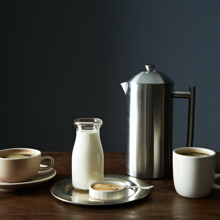 a table topped with two cups of coffee next to a pitcher and plate filled with cookies