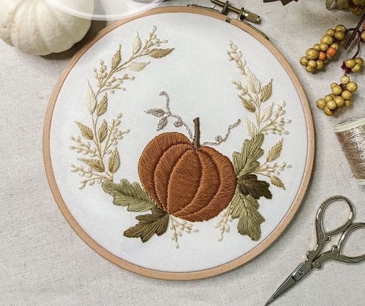 an embroidered pumpkin surrounded by autumn leaves and other crafting supplies on a white table