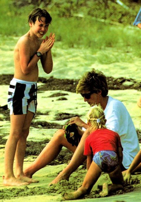 three people sitting on the beach and one person standing in the sand with their hands together