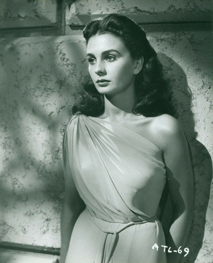 an old photo of a woman in a dress standing next to a stone wall with her hands on her hips