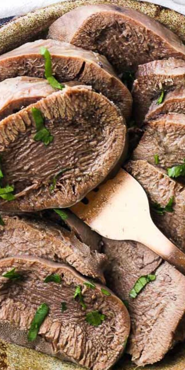 sliced meat with parsley on top in a bowl next to a wooden spatula