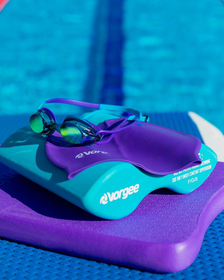 a pair of swimming goggles sitting on top of a purple mat next to a pool