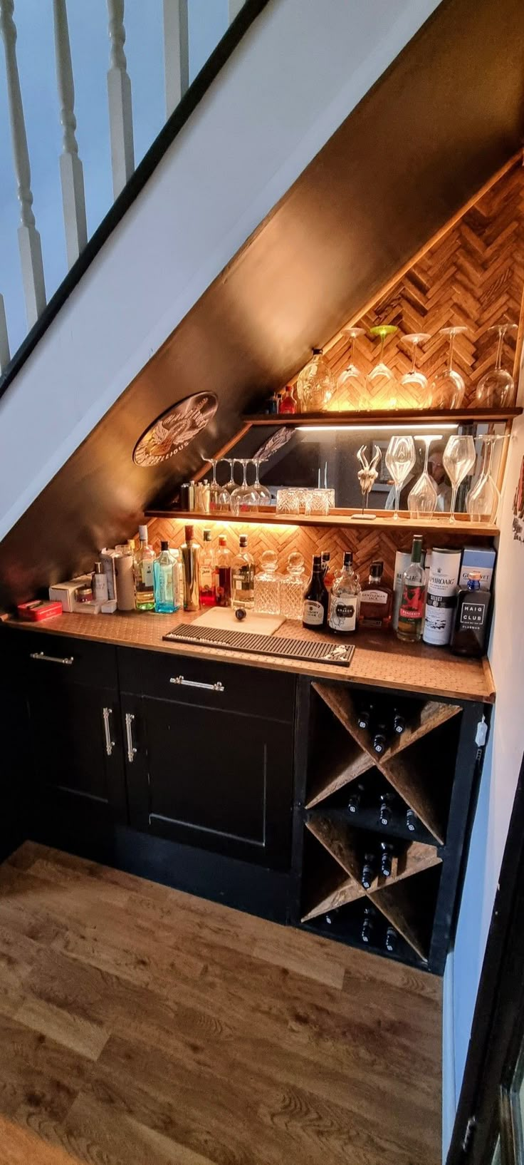 a kitchen under a stair case with wine glasses and bottles on the top shelf in front of it