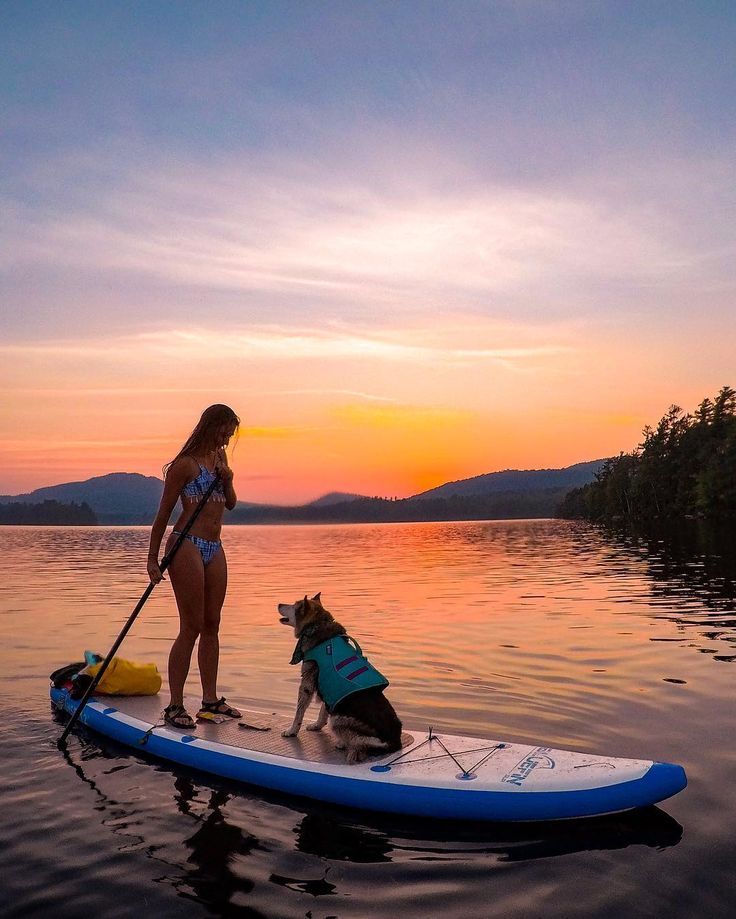 a woman and her dog on a paddle board in the water as the sun sets