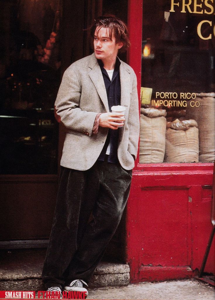 a man standing in front of a store holding a coffee cup and looking at the camera