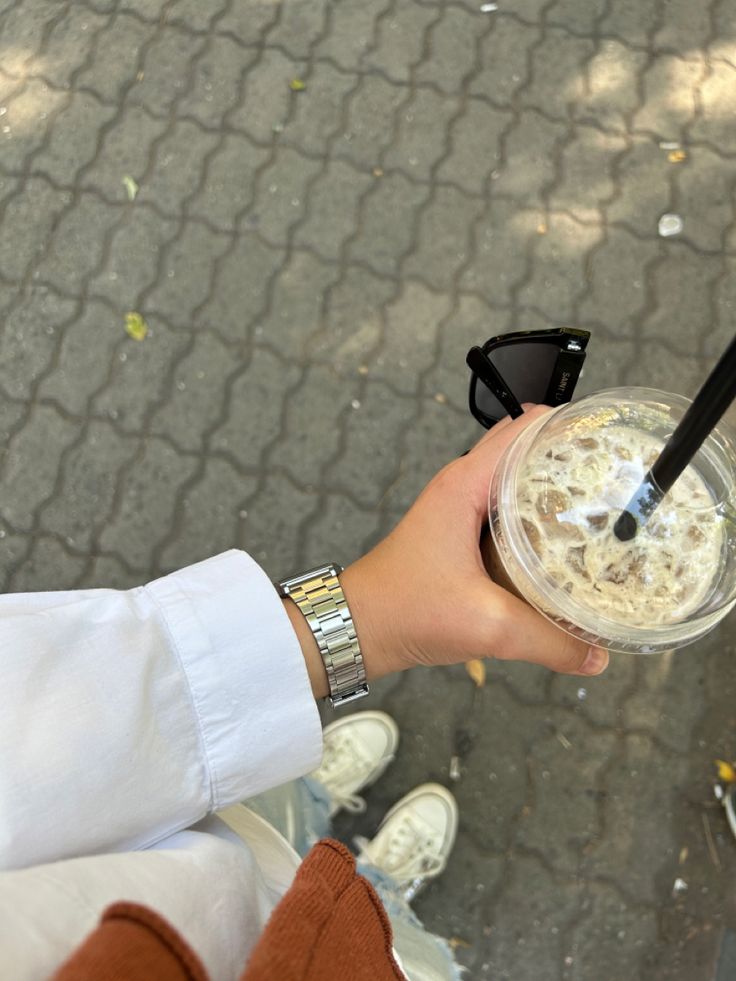 a person holding a drink in their hand on the ground with other people standing around