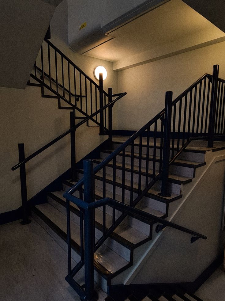 an empty stairwell with metal handrails and lights on the wall behind it,