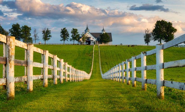 a white fence is in front of a green field with a church on the hill