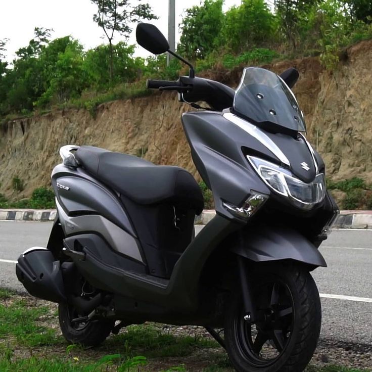 a black scooter parked on the side of the road next to a hill