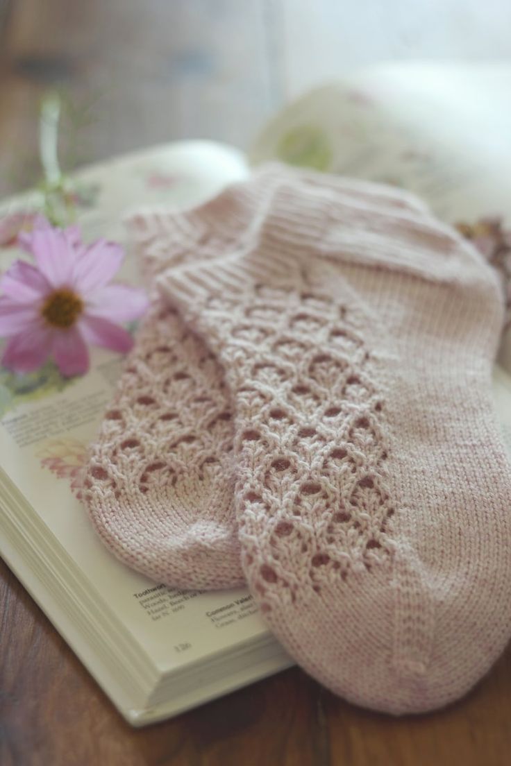 a pair of pink knitted socks sitting on top of a book next to a flower